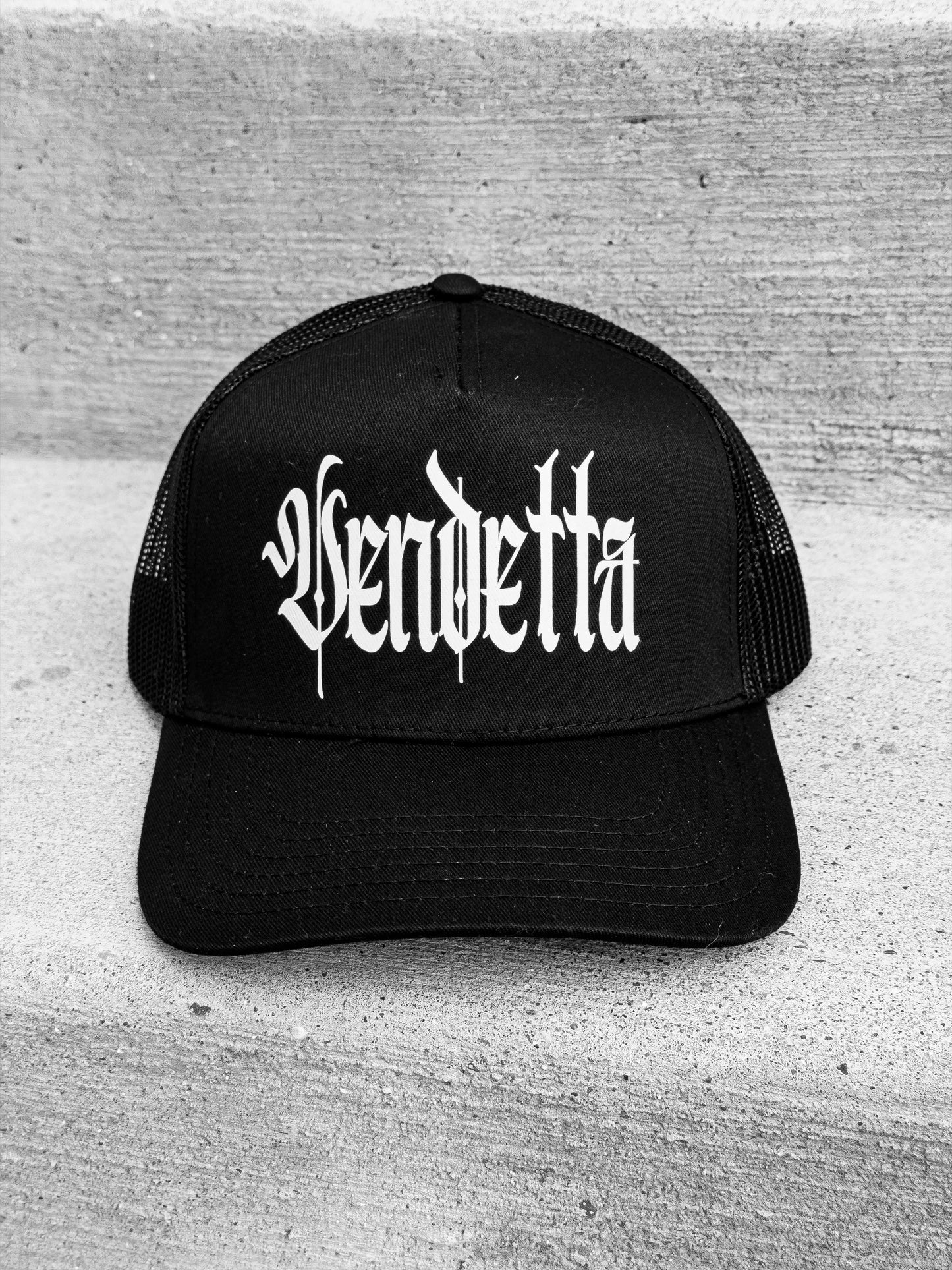 Fitted for vendetta - Black vendetta trucker hat - front view on concrete 